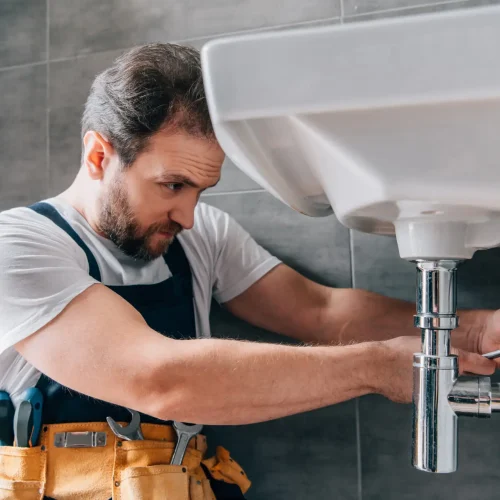 focused male plumber in working overall fixing sink in bathroom