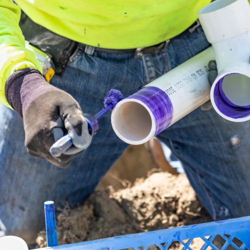 Plumber Applying Pipe Cleaner, Primer and Glue to PVC Pipe At Construction Site.
