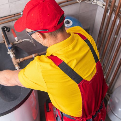 Professional Caucasian Plumber Repairing Tank Water Heater in Boiler Room of Commercial Building. Heating Equipment Maintenance Theme.